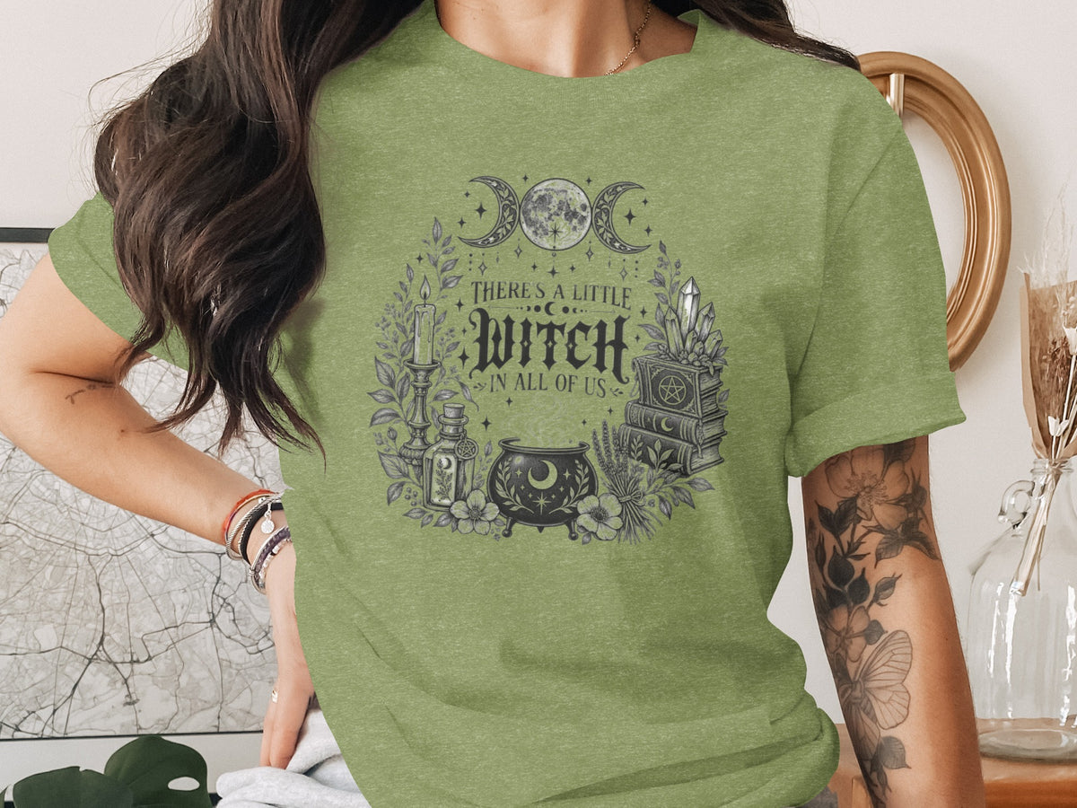 A person wearing a green t-shirt with a vintage graphic that reads "There's a little witch in all of us."