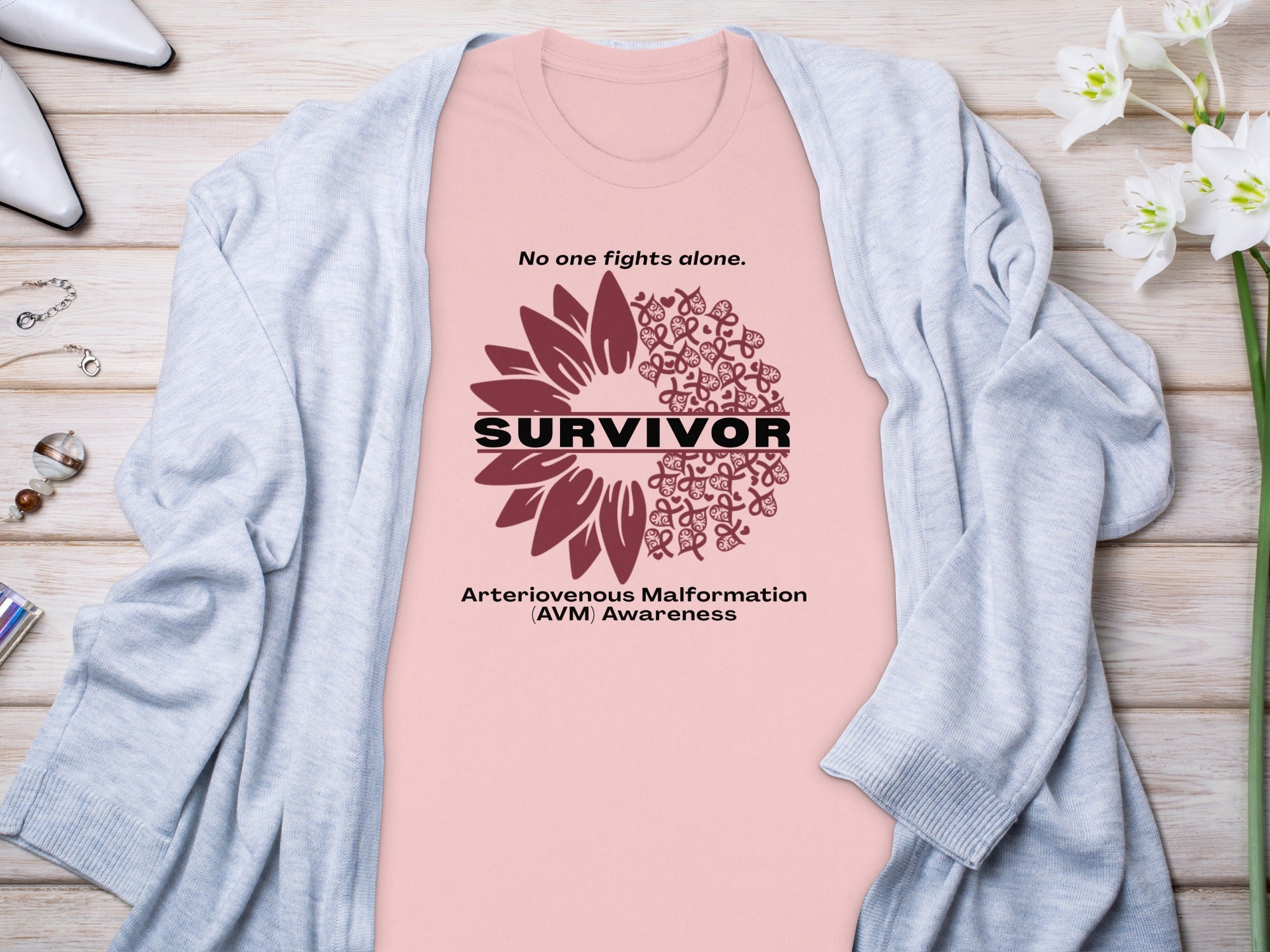 Pink t-shirt with "Survivor" text, sunflower design, and "AVM Awareness" slogan.