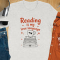 T-shirt with "Reading is my love language" text over stacked books and a coffee cup.