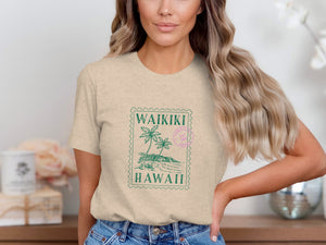 Tan t-shirt with green Waikiki Hawaii stamp graphic featuring palm trees and mountains.