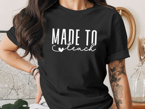 Black t-shirt with white text "MADE TO teach" and a heart.