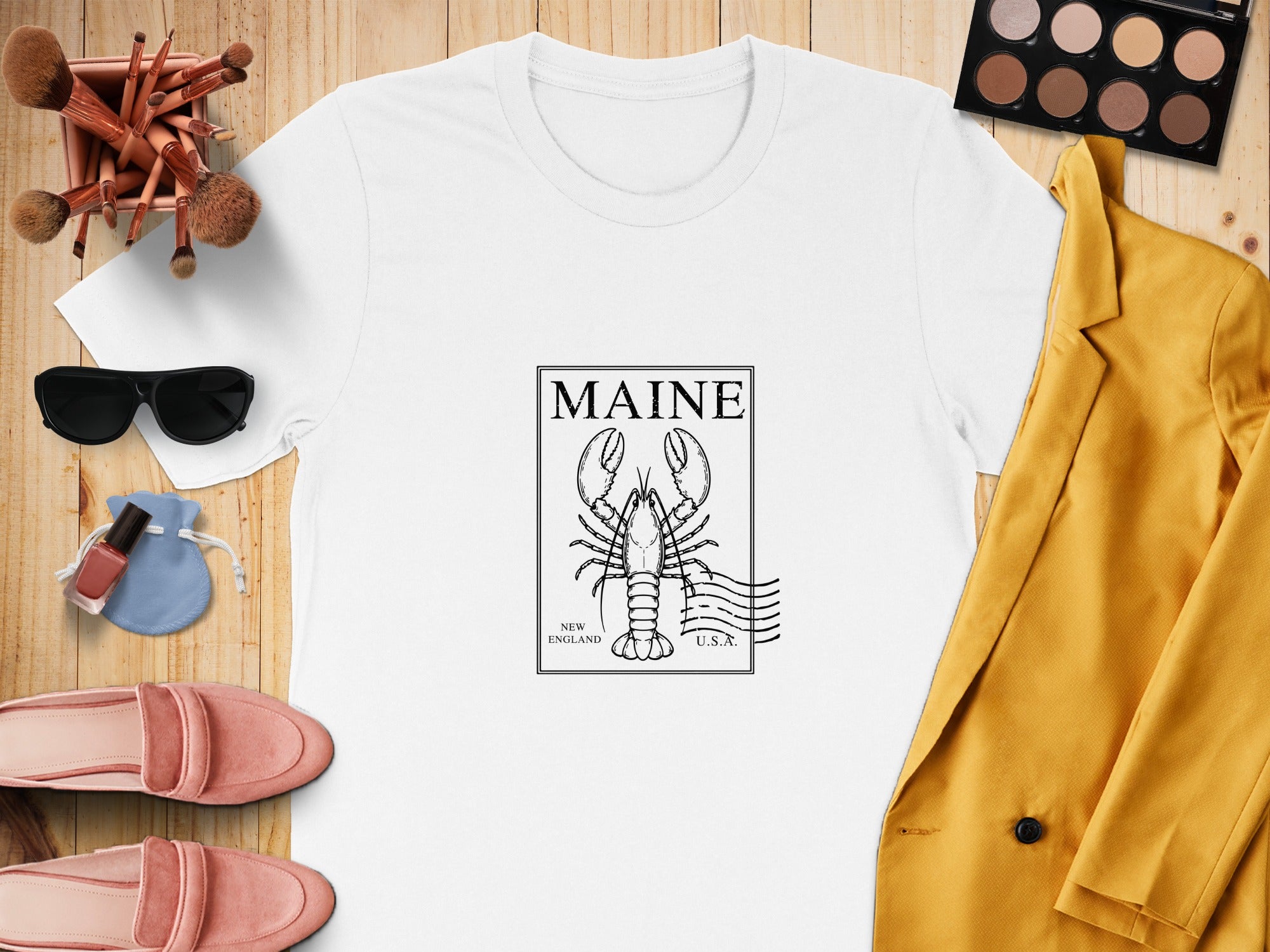 White t-shirt with Maine lobster stamp graphic, surrounded by makeup and clothing accessories.
