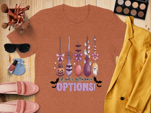 Orange t-shirt with Halloween brooms, ghosts, bats, and text "A girl's gotta have OPTIONS!".