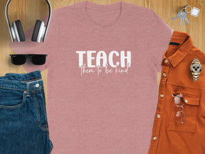 Pink t-shirt with "TEACH them to be kind" text, flat lay with jeans, headphones.