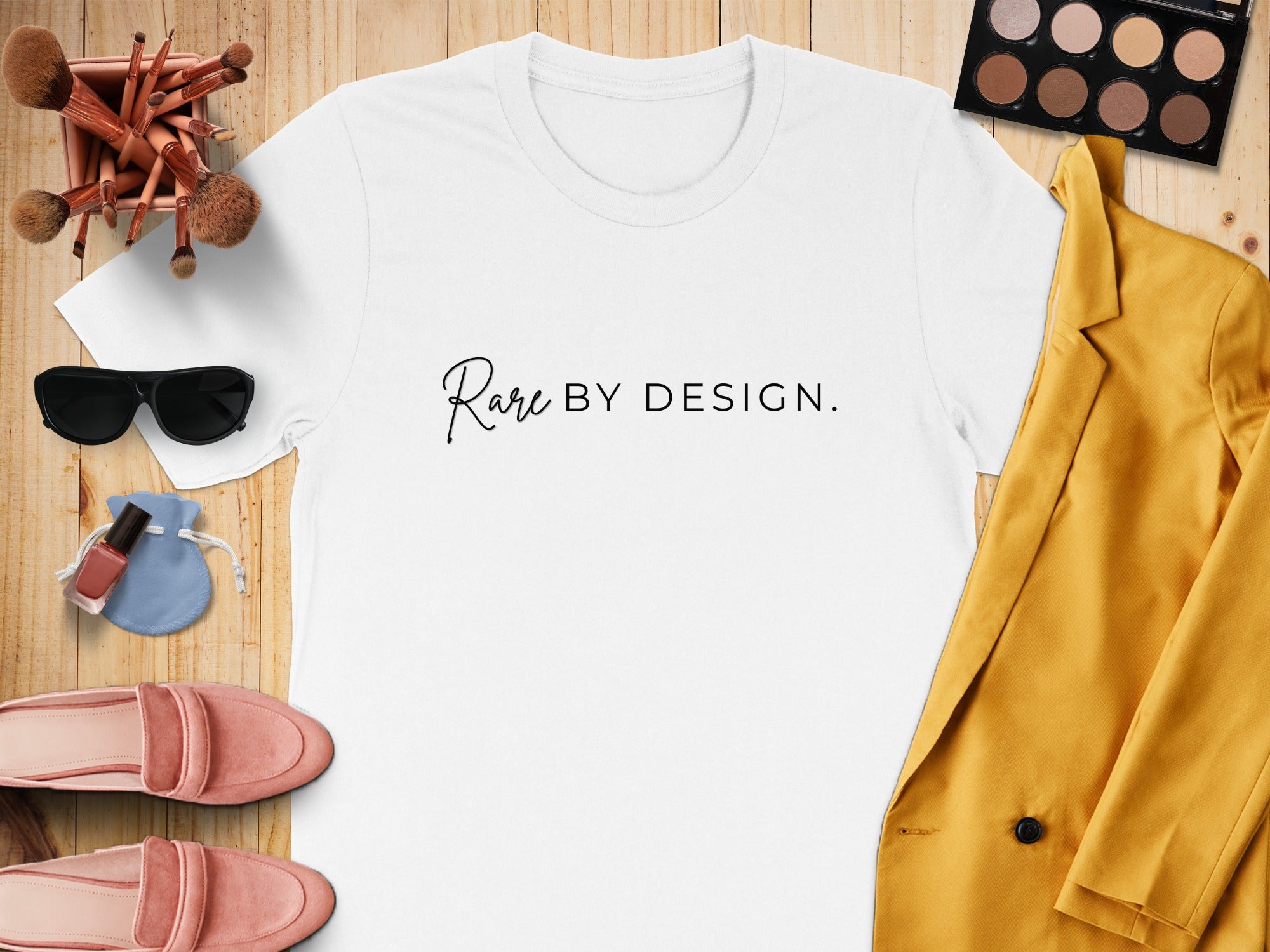 White t-shirt with "Rare BY DESIGN." slogan, surrounded by makeup and accessories.
