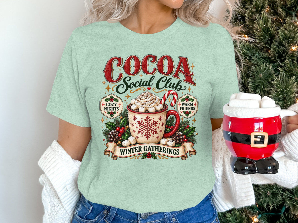 Light green t-shirt graphic with "Cocoa Social Club" and hot cocoa mug.