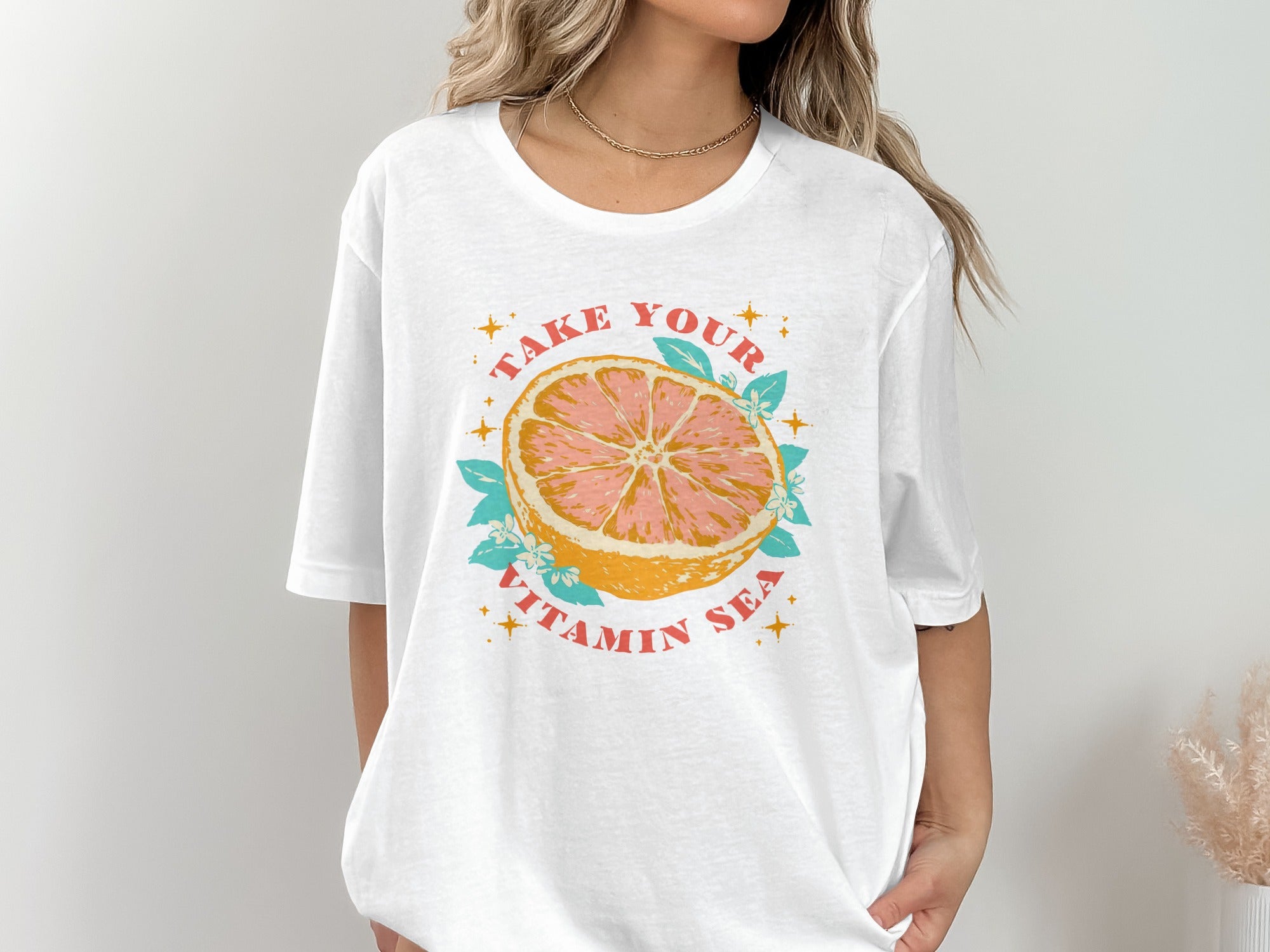 White graphic t-shirt with a grapefruit slice illustration and the text "TAKE YOUR VITAMIN SEA".