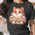 Cartoon cat holds wooden sign reading "FOOD LOVER" on dark grey t-shirt.