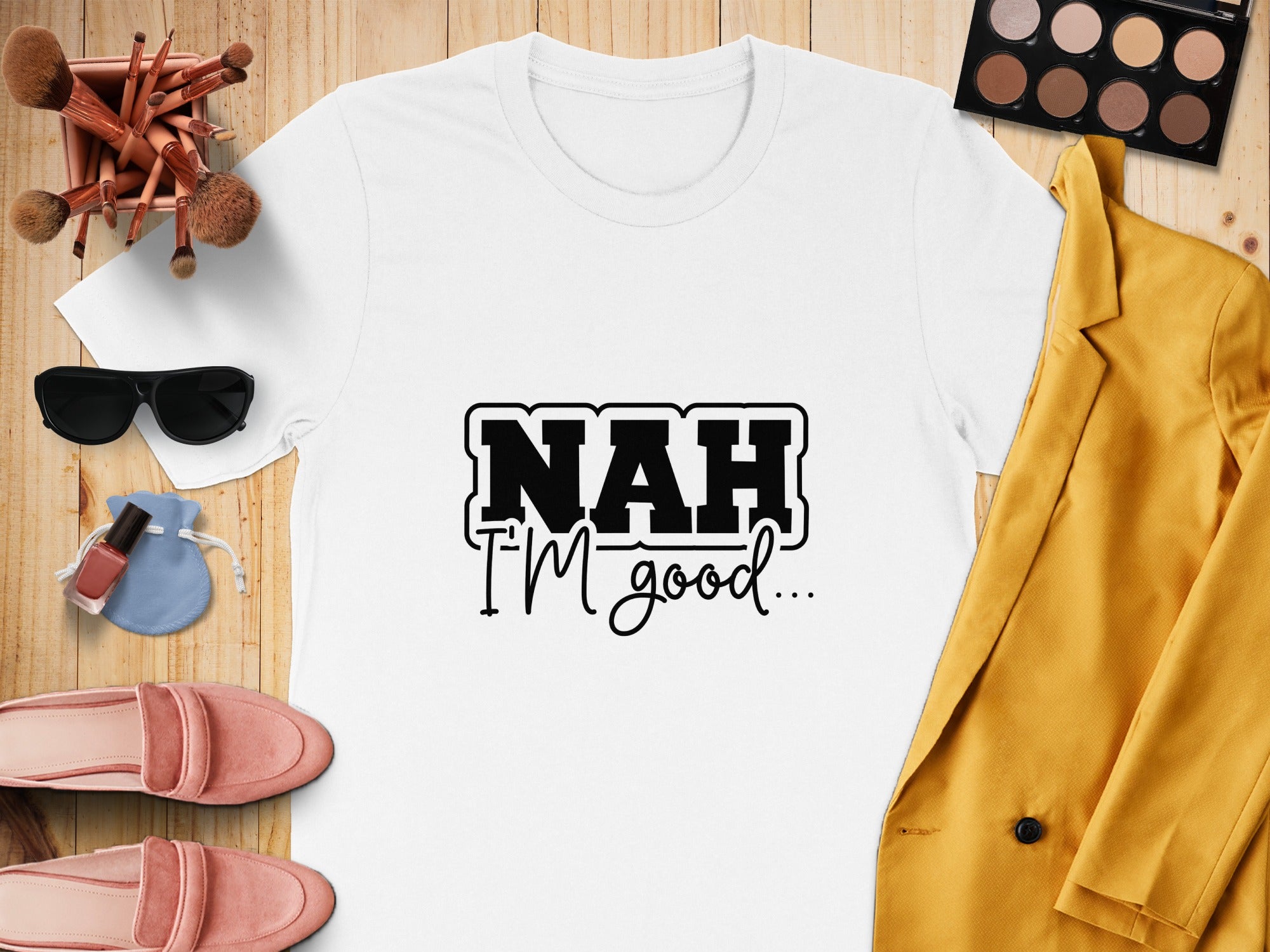 White t-shirt with "NAH I'M good..." text, flat lay with makeup and fashion items.