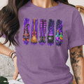 Purple t-shirt with Halloween witchy graphic: hat, broom, legs, cauldron, and potions.
