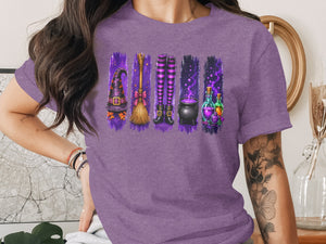 Purple t-shirt with Halloween witchy graphic: hat, broom, legs, cauldron, and potions.