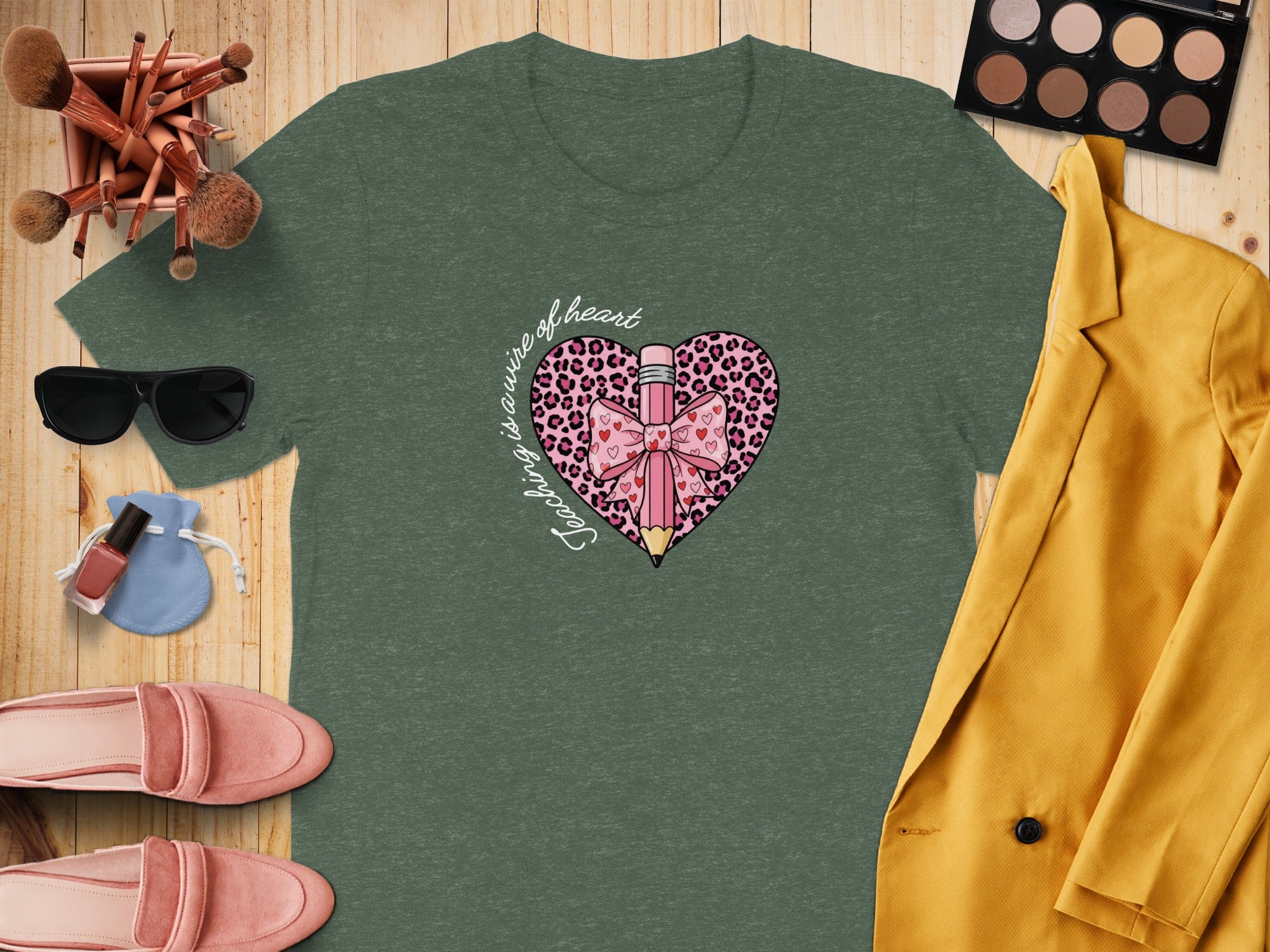 Green t-shirt with pink leopard print heart and pencil graphic that says "Teaching is a work of heart".