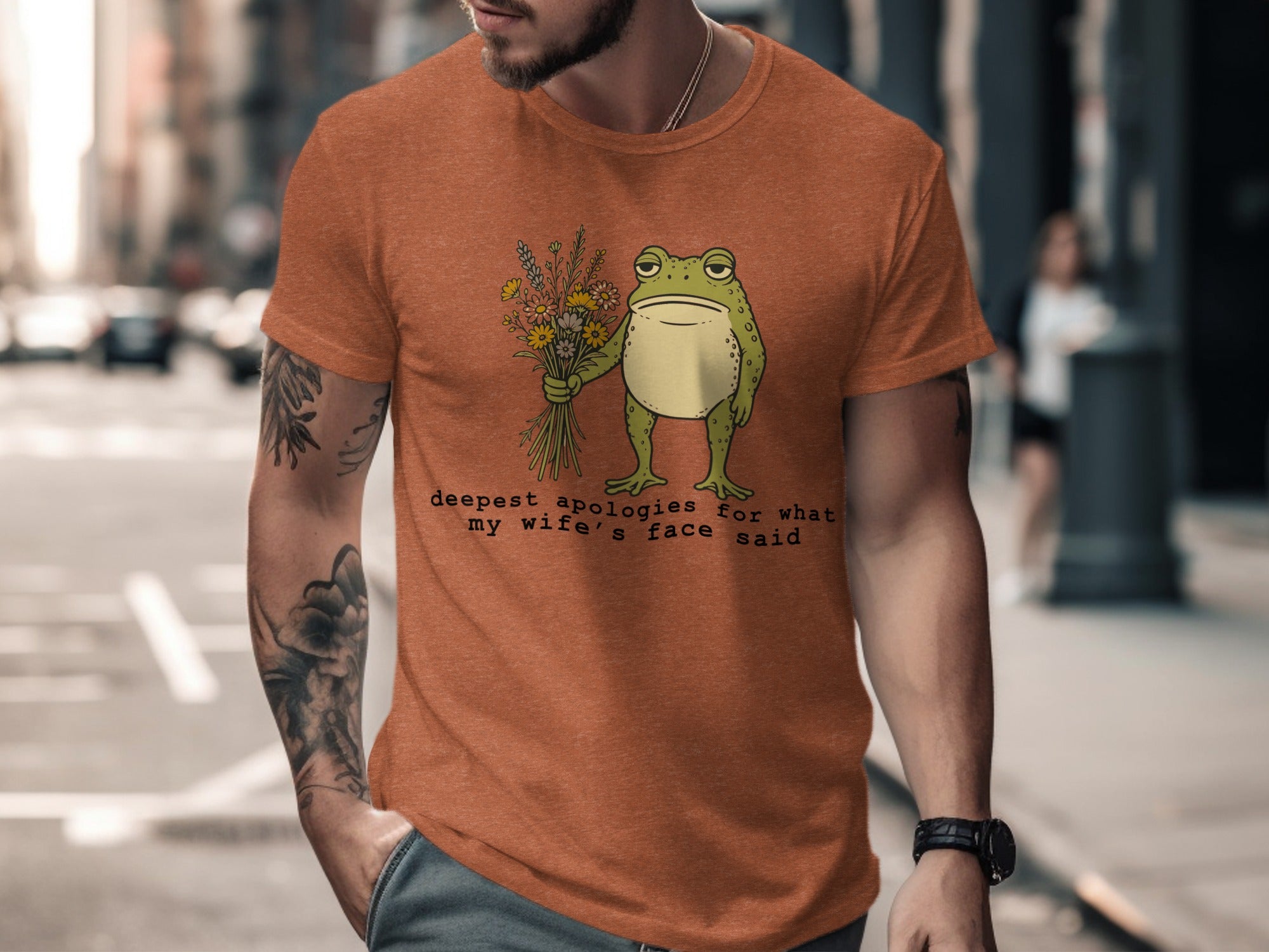 Orange t-shirt with a sad frog holding flowers and text about wife's face.
