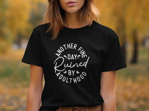 Black t-shirt with white text reading "Another fine day ruined by adulthood"