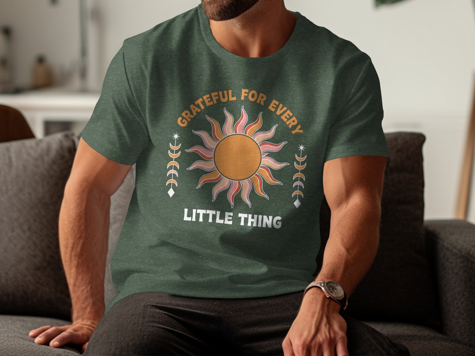 Green t-shirt with a graphic of a stylized sun and moons, reading "Grateful For Every Little Thing."