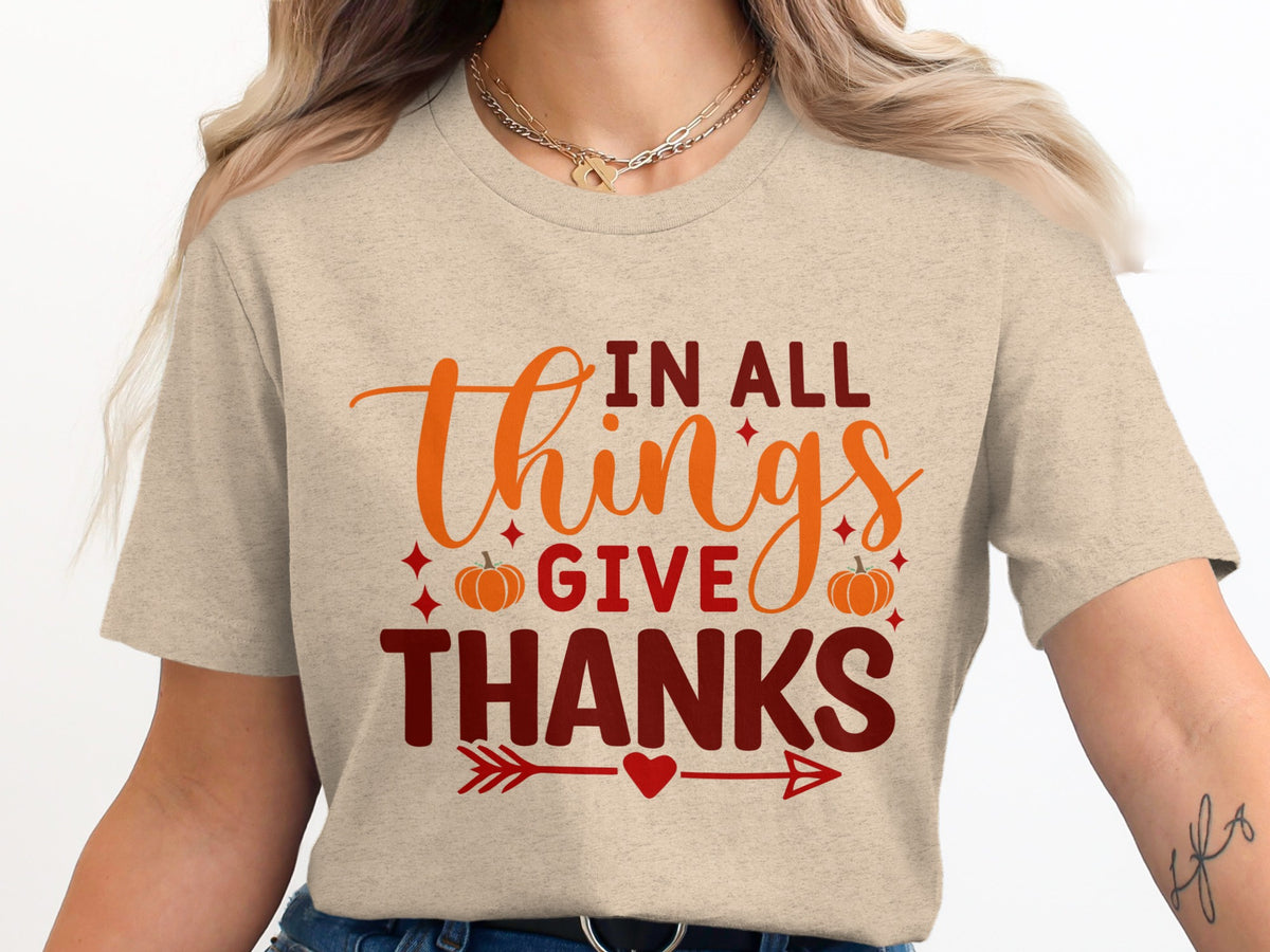 "In All Things Give Thanks" text with pumpkins and arrows on a tan shirt.
