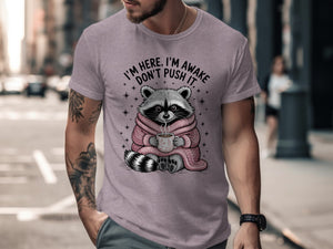 Raccoon in pink sweater holding coffee mug with text "I'm here, I'm awake, don't push it."