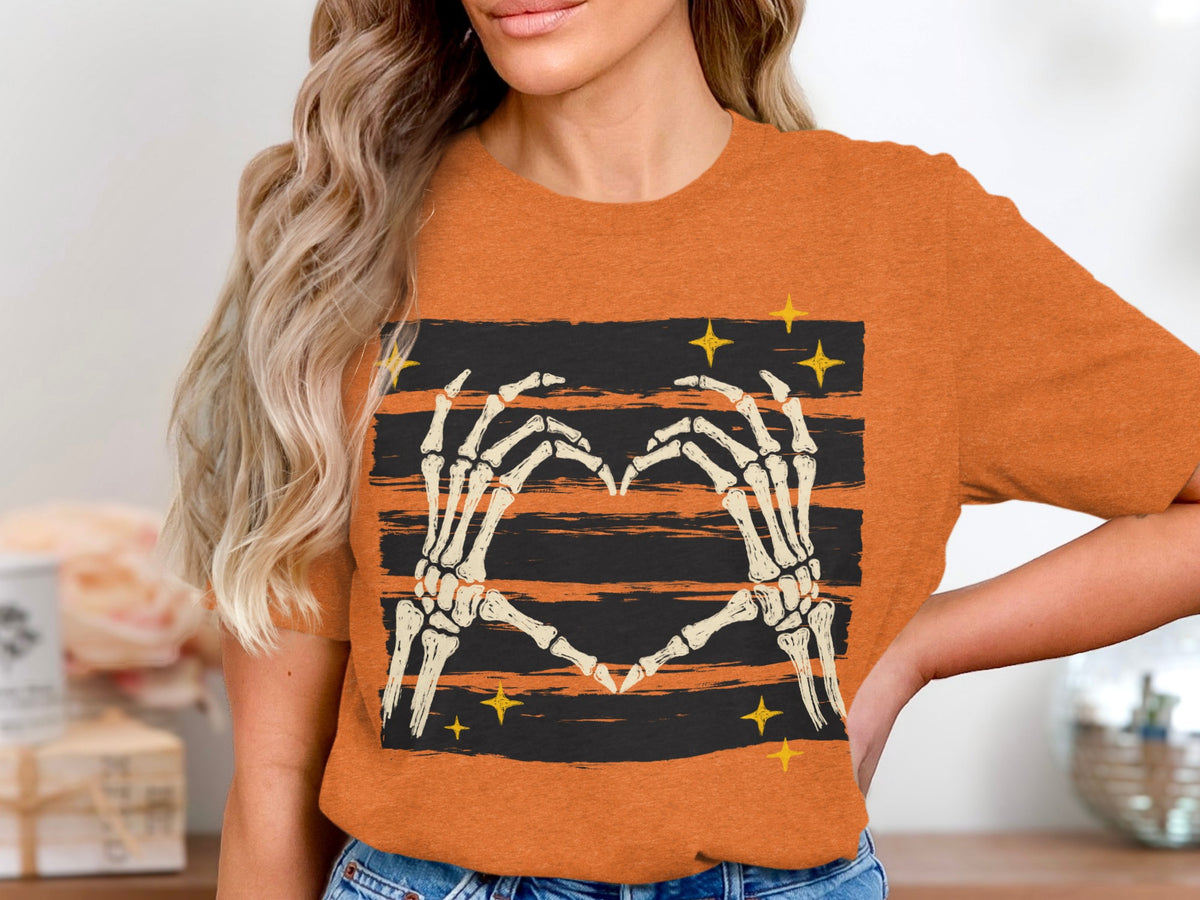 Skeleton hands form a heart on an orange t-shirt with black stripes and yellow stars.