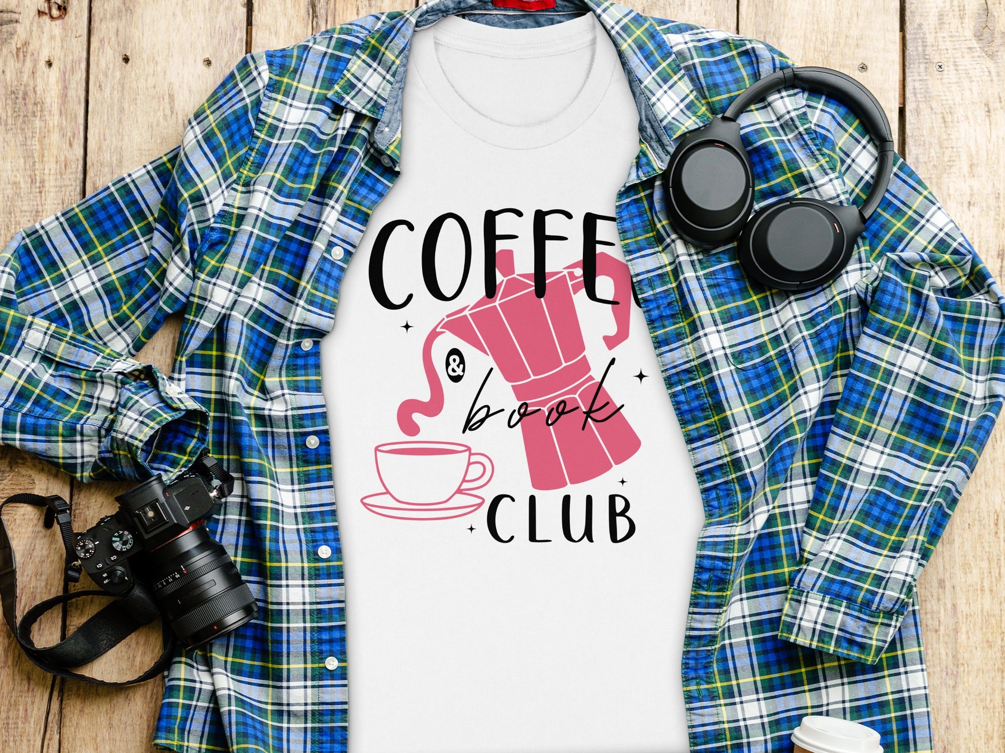 White t-shirt with "Coffee & Book Club" design, laying on wooden planks with a flannel shirt.