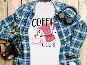 White t-shirt with "Coffee & Book Club" design, laying on wooden planks with a flannel shirt.