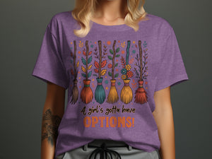 Purple t-shirt with brooms decorated with leaves and flowers. Text: "A girl's gotta have OPTIONS!"