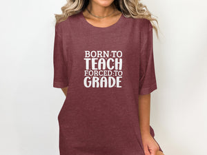 Maroon t-shirt with white text that reads "BORN TO TEACH FORCED TO GRADE".