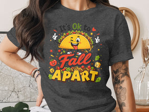 Taco graphic with text "It's Ok to Fall Apart" on dark grey t-shirt.