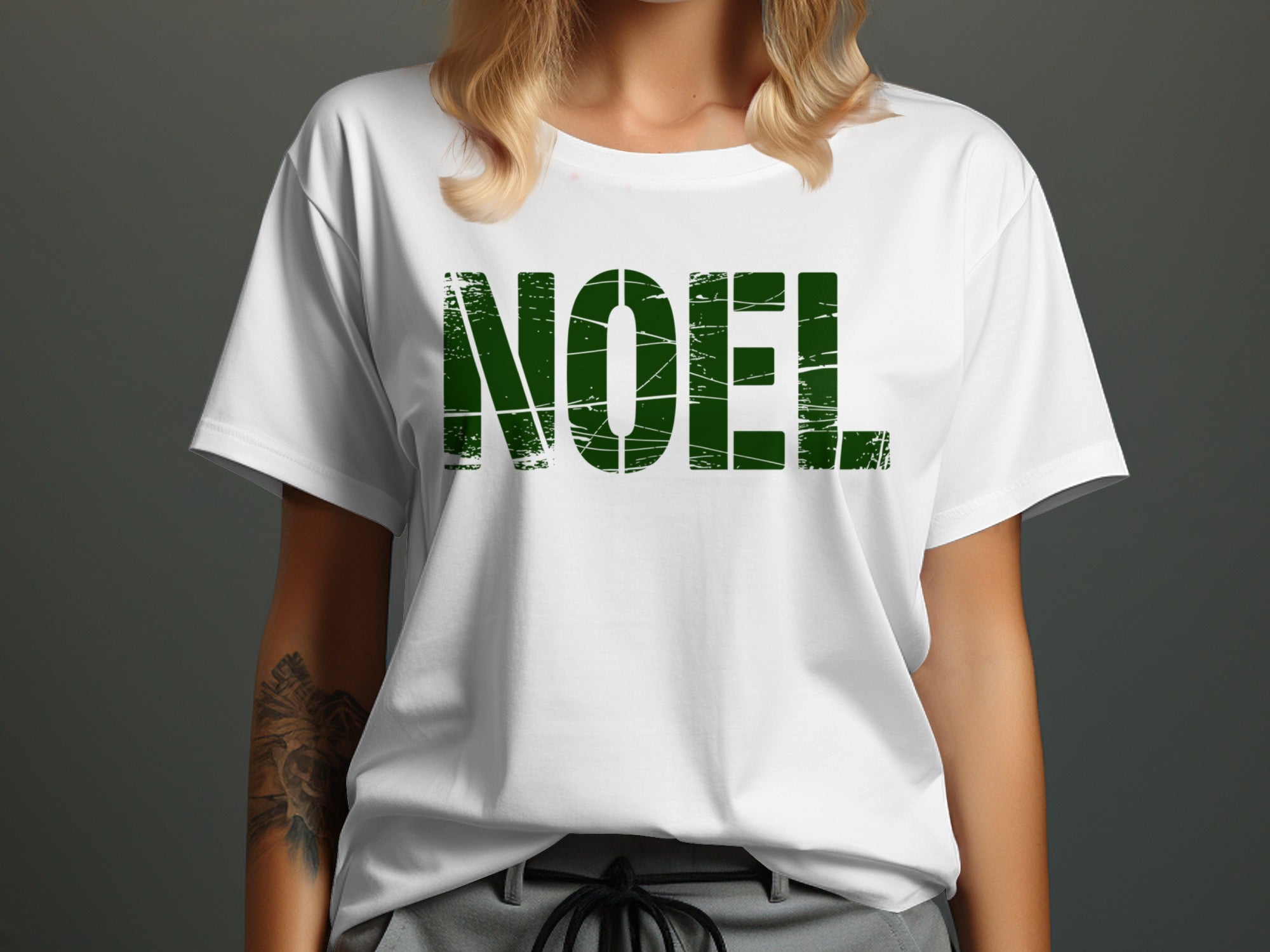 White t-shirt with distressed green "NOEL" text and a woman's shoulder and arm.
