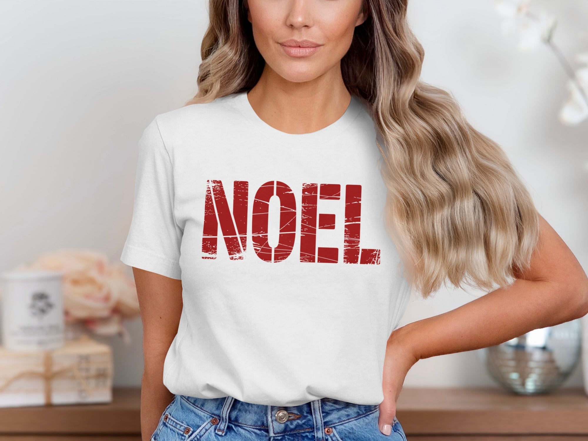 Woman wearing white t-shirt with distressed red "NOEL" text.
