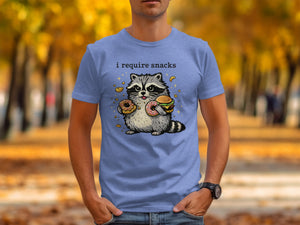 Blue t-shirt with a raccoon holding donuts and a burger, text says "i require snacks".