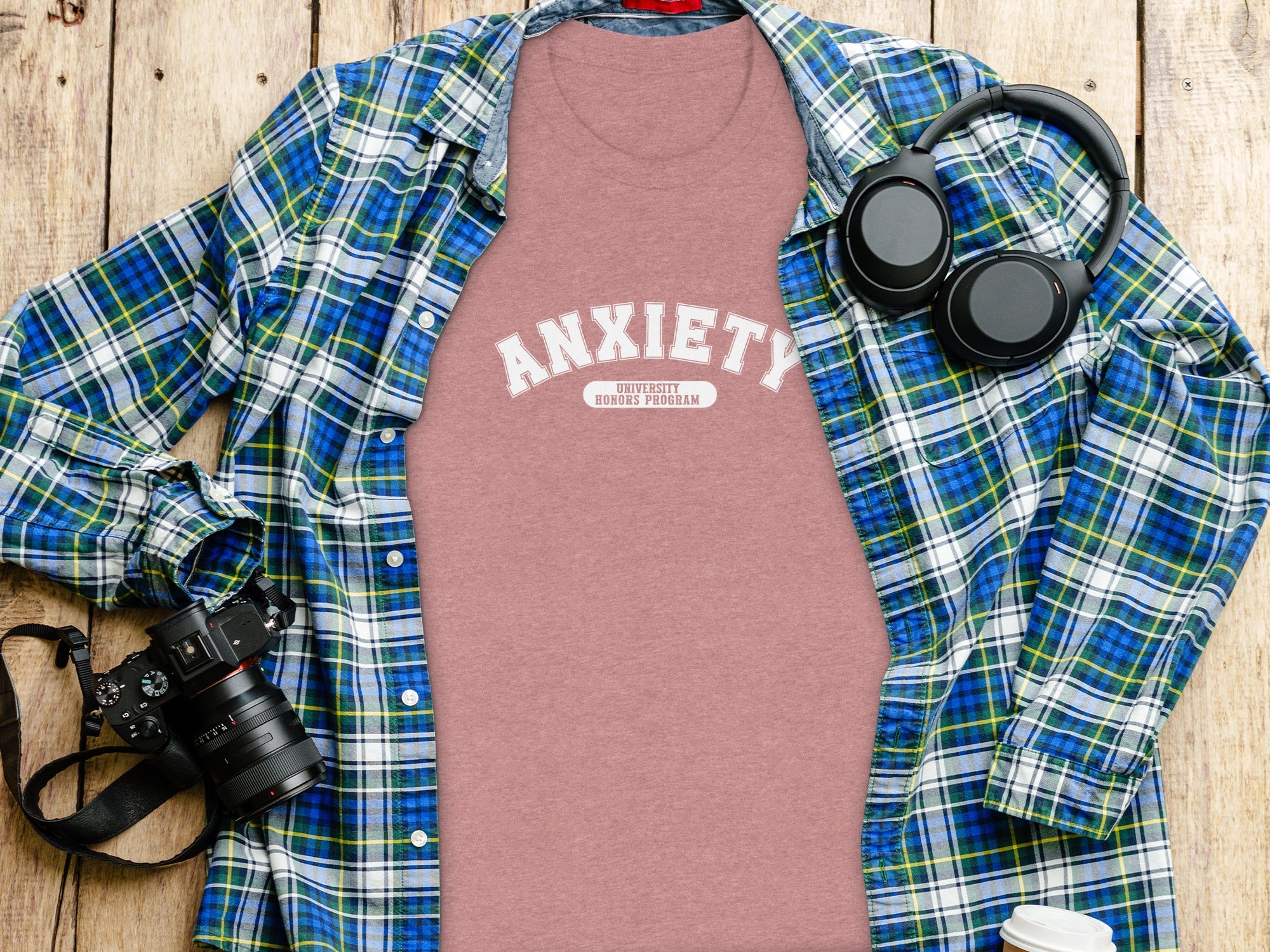 Pink t-shirt with "ANXIETY UNIVERSITY HONORS PROGRAM" text, a plaid shirt, headphones, and camera.