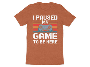 Orange t-shirt with text "I PAUSED MY GAME TO BE HERE" and game controller graphic.