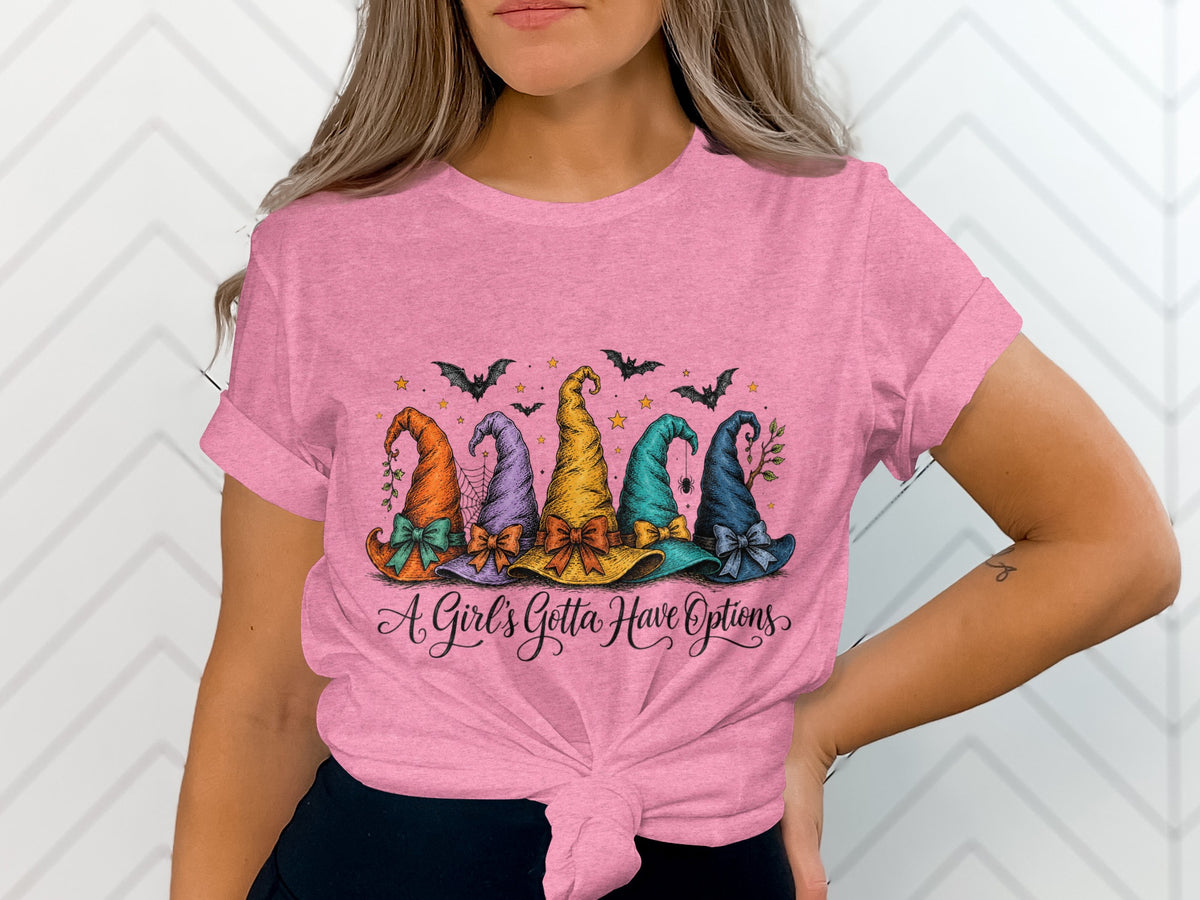 Pink t-shirt with five colorful witch hats and text that reads "A Girl's Gotta Have Options".