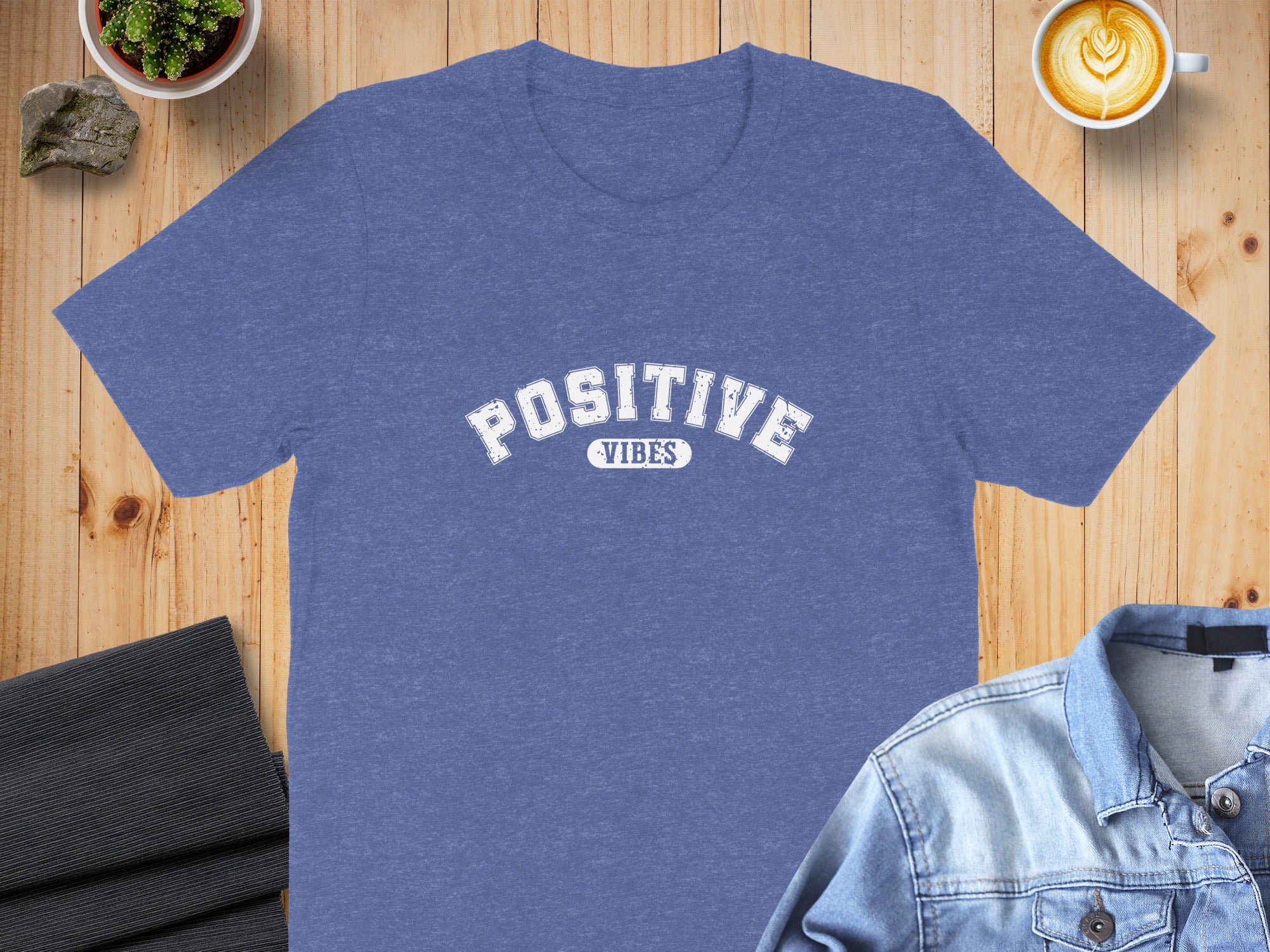 Blue t-shirt with white "POSITIVE VIBES" text on a wooden background.