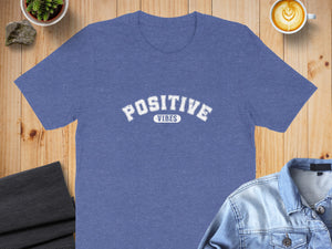 Blue t-shirt with white "POSITIVE VIBES" text on a wooden background.