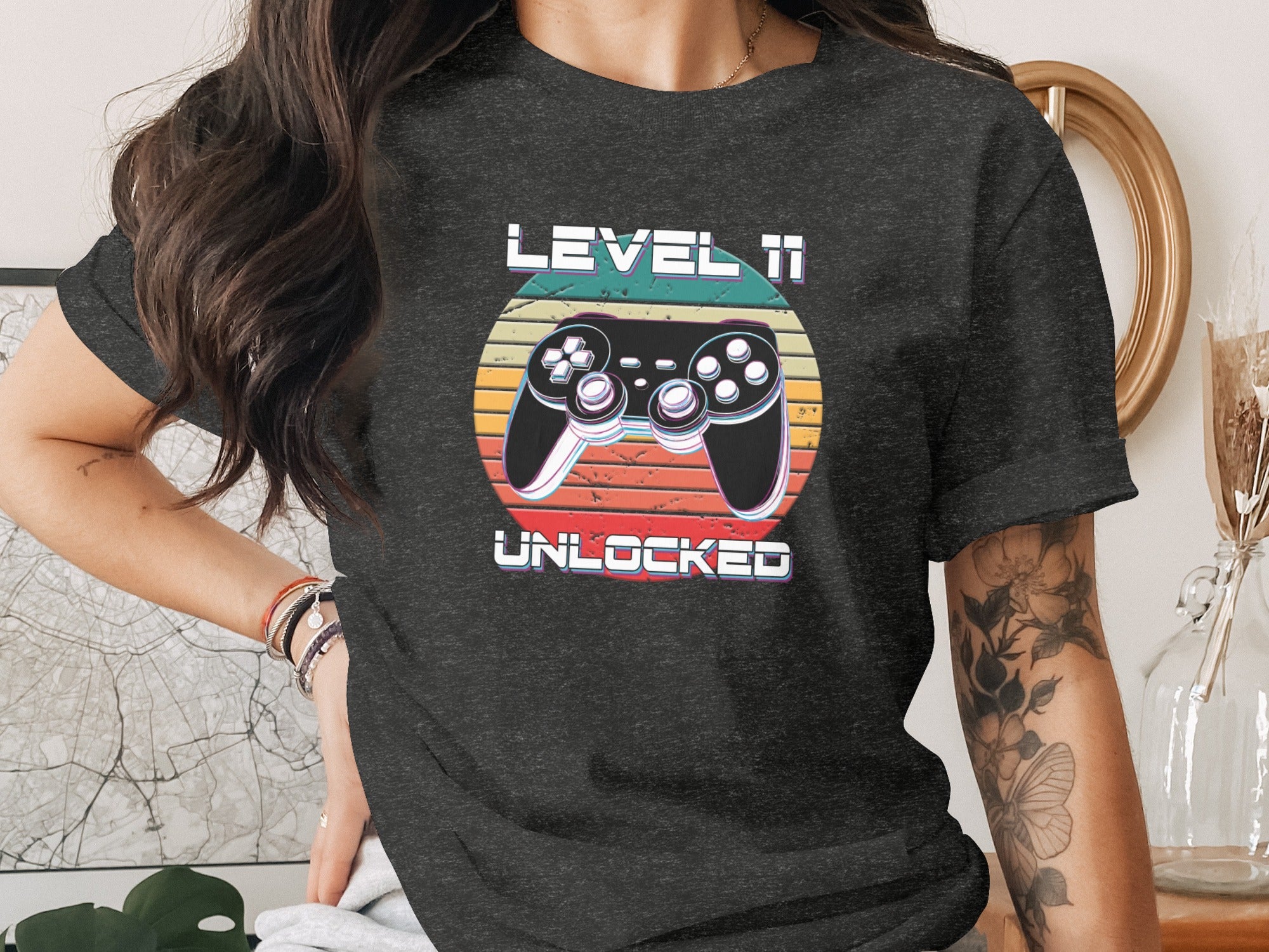 "Level 11 Unlocked" text with retro joystick and sunset background on a dark t-shirt.