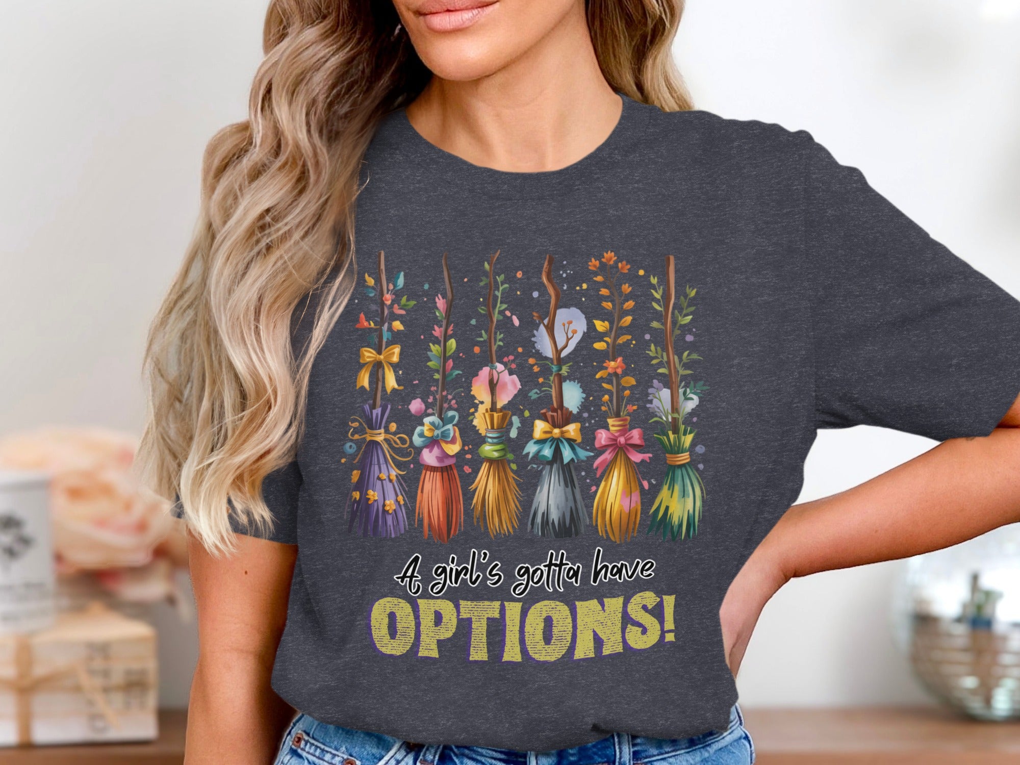 Dark gray t-shirt with a graphic of decorative brooms and text reading "A girl's gotta have OPTIONS!"