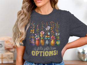 Dark gray t-shirt with a graphic of decorative brooms and text reading "A girl's gotta have OPTIONS!"