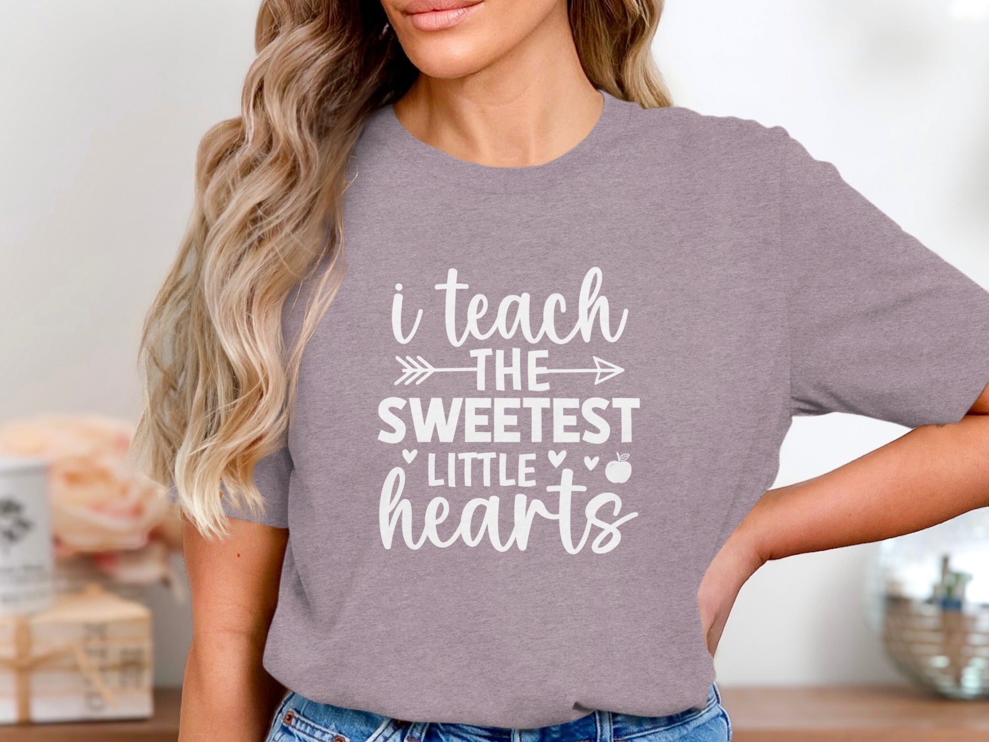 Purple t-shirt with white text "i teach the sweetest little hearts" and an apple.