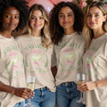 Four women wearing matching oatmeal-colored t-shirts that read Margarita Girls Social Club stand together.