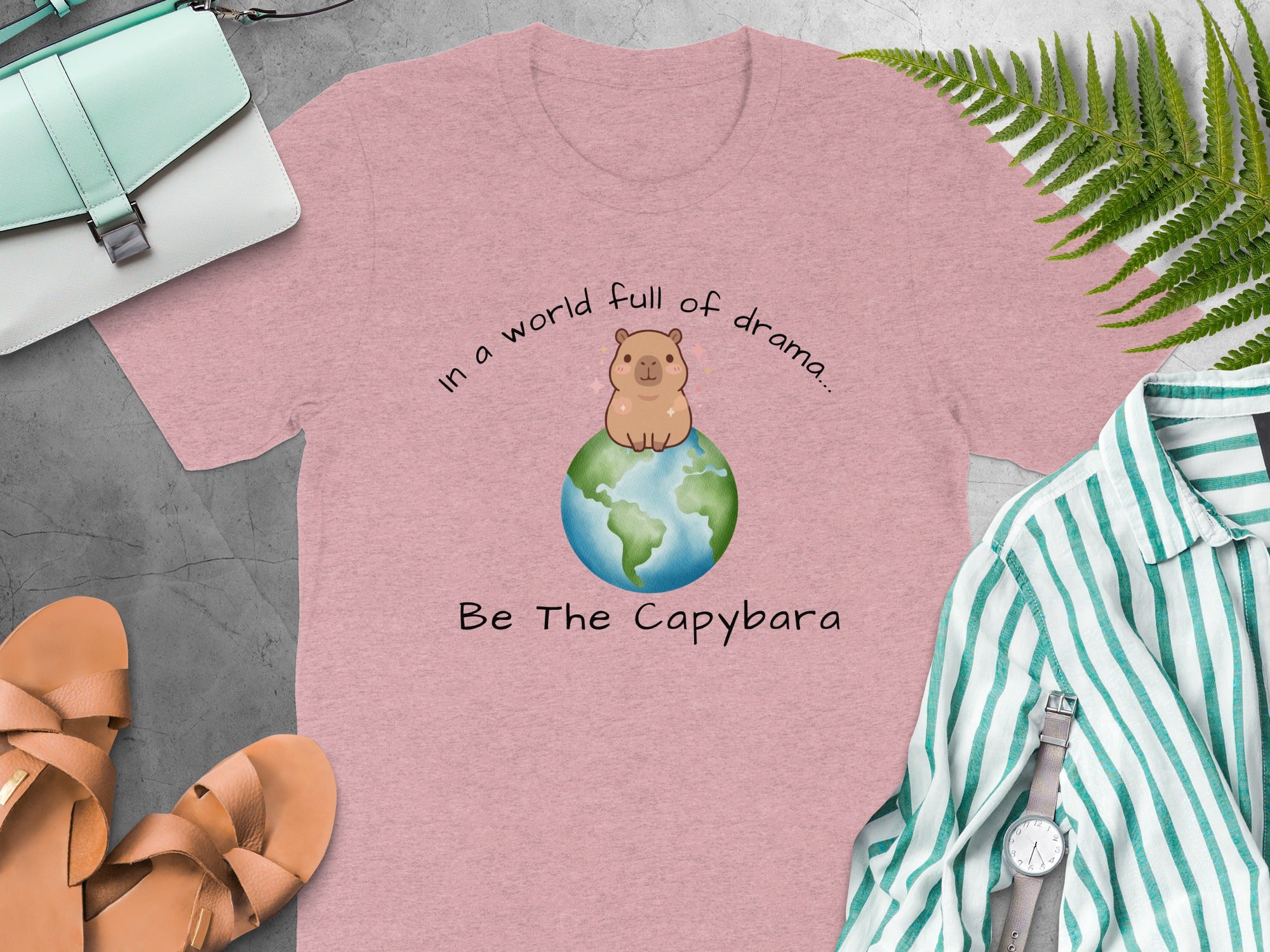 Pink t-shirt with a capybara on the Earth and text "In a world full of drama... Be The Capybara."