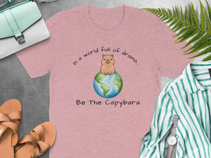 Pink t-shirt with a capybara on the Earth and text "In a world full of drama... Be The Capybara."