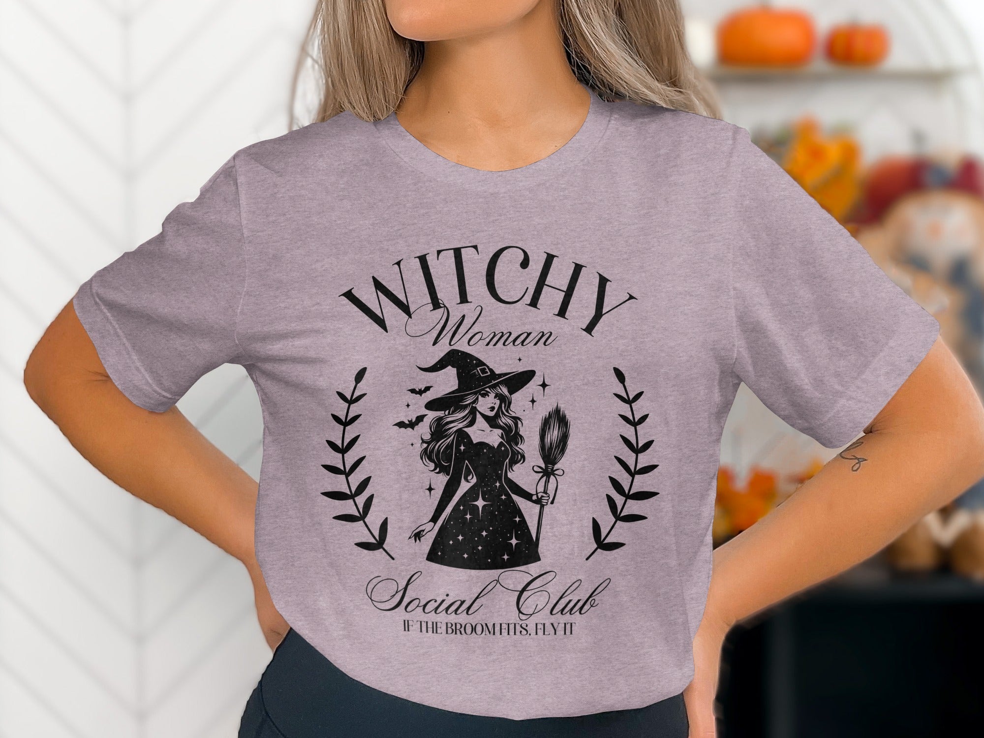 Light purple t-shirt with black graphic of a witch, bats, and text "Witchy Woman Social Club".