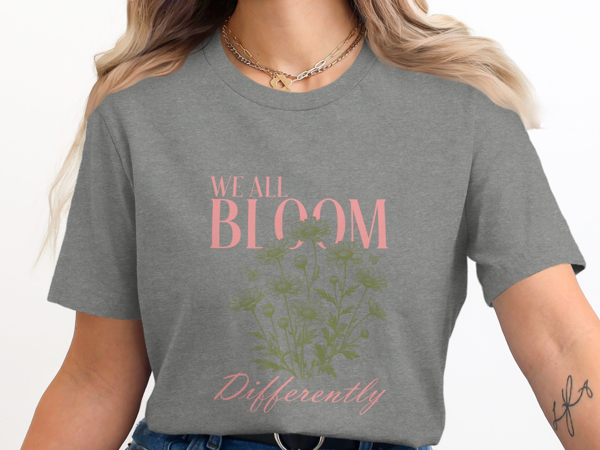 Grey t-shirt with "WE ALL BLOOM Differently" text and green floral graphic.