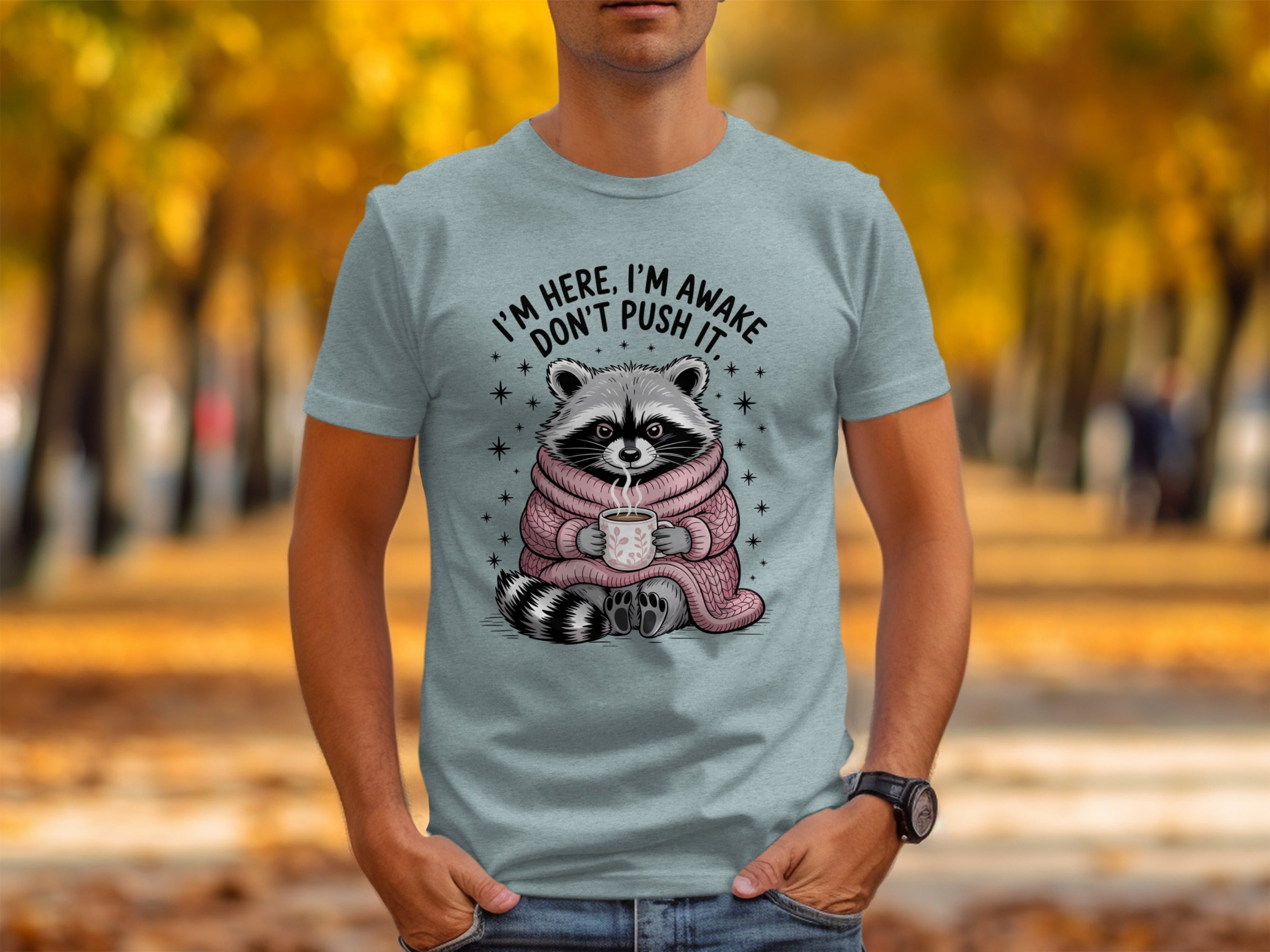 Raccoon wearing a pink sweater holding a mug with text "I'M HERE, I'M AWAKE DON'T PUSH IT."