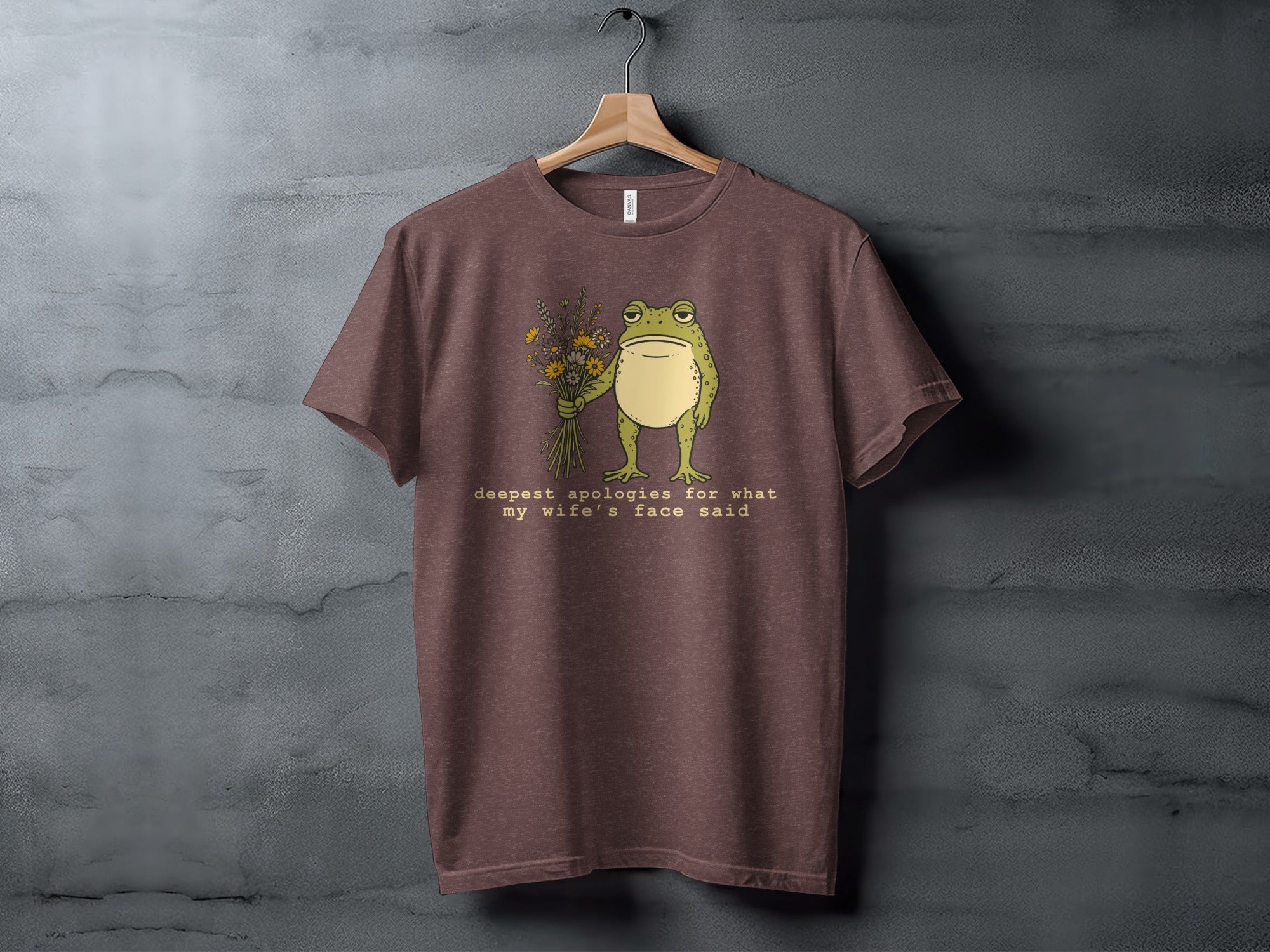Brown t-shirt with a frog holding flowers and the text "deepest apologies for what my wife's face said."