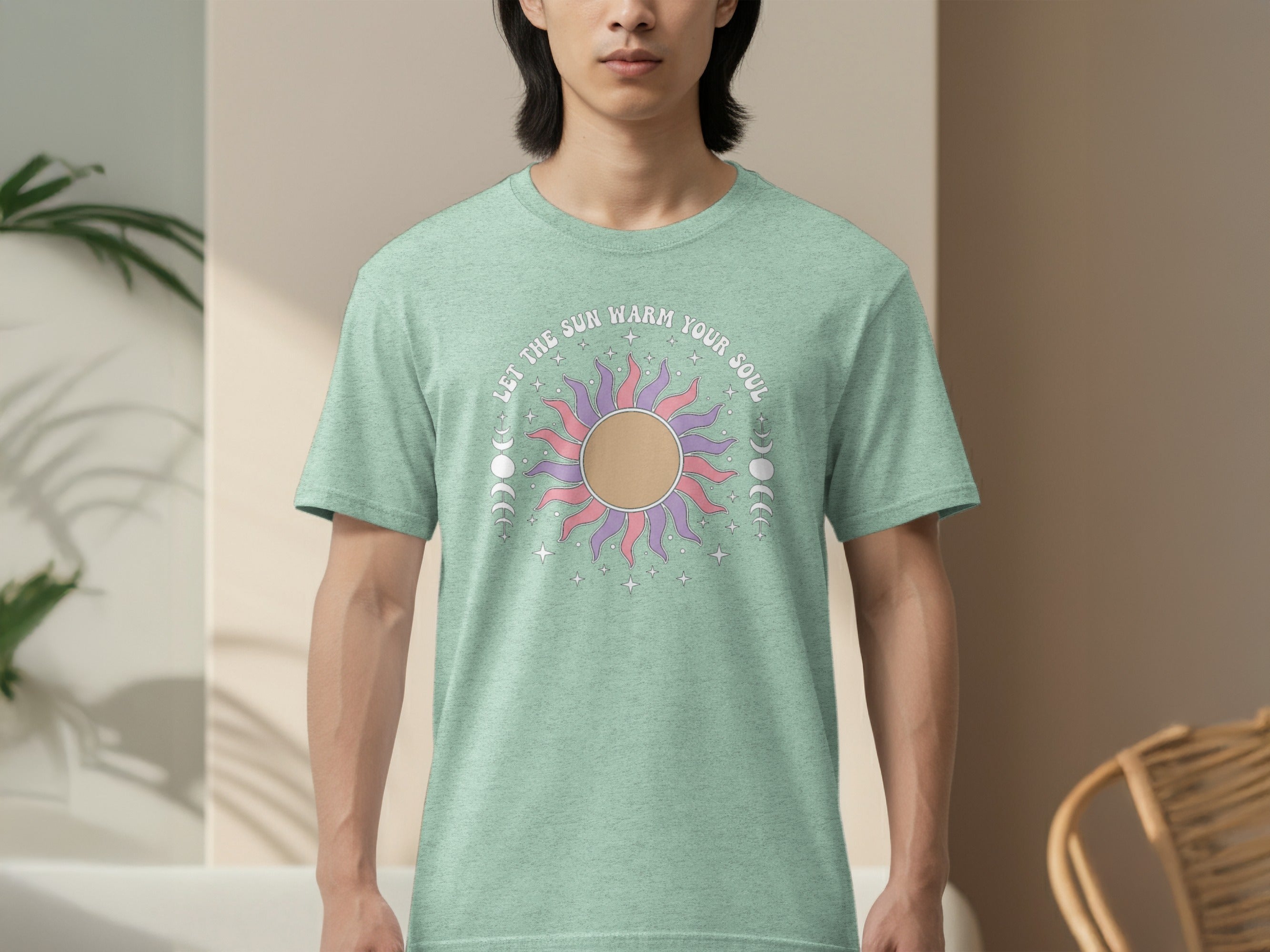 Green t-shirt with a sun, moon phases, and stars graphic saying "Let the sun warm your soul."