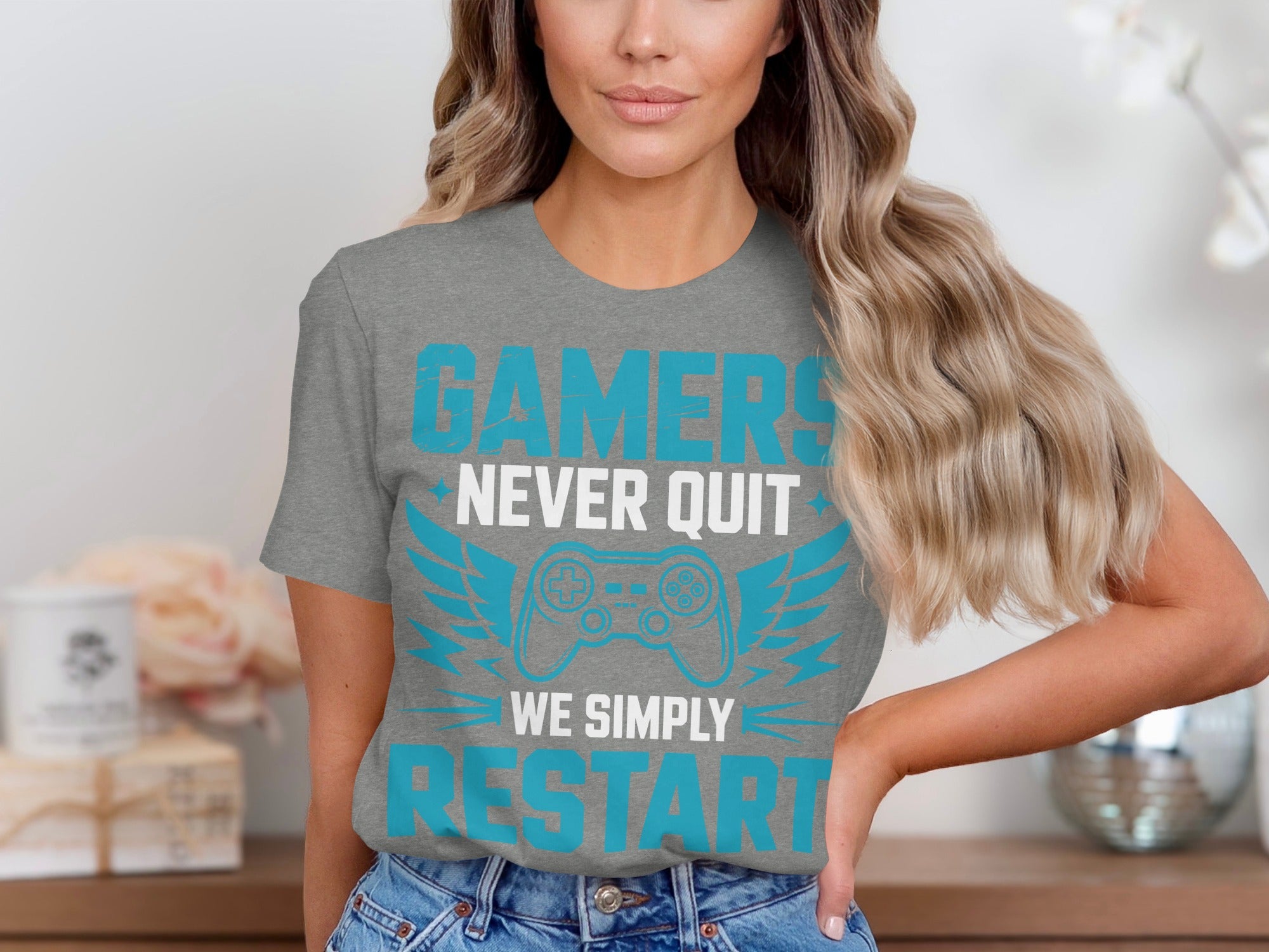 Grey t-shirt with text "GAMERS NEVER QUIT WE SIMPLY RESTART" and a video game controller graphic.