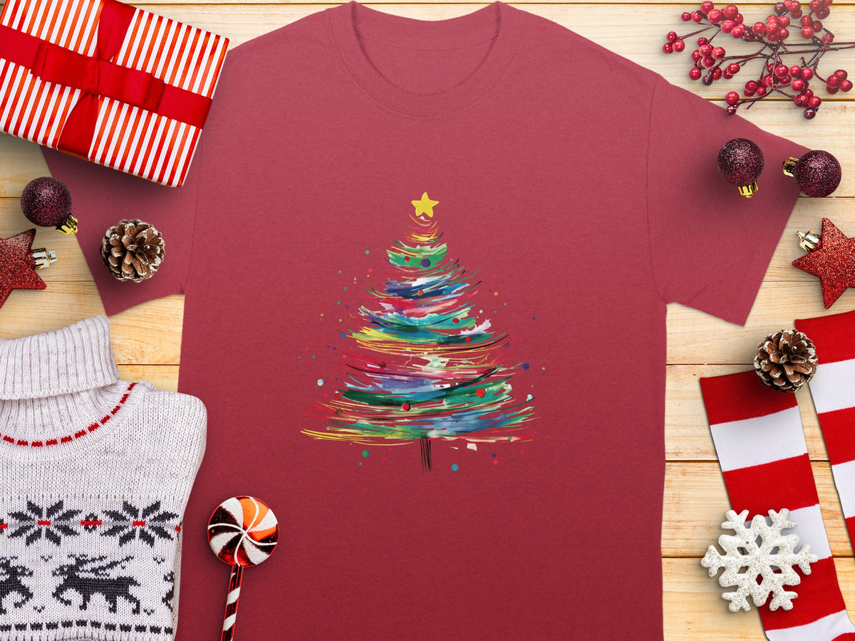 Crimson t-shirt with watercolor Christmas tree graphic, surrounded by festive decorations.