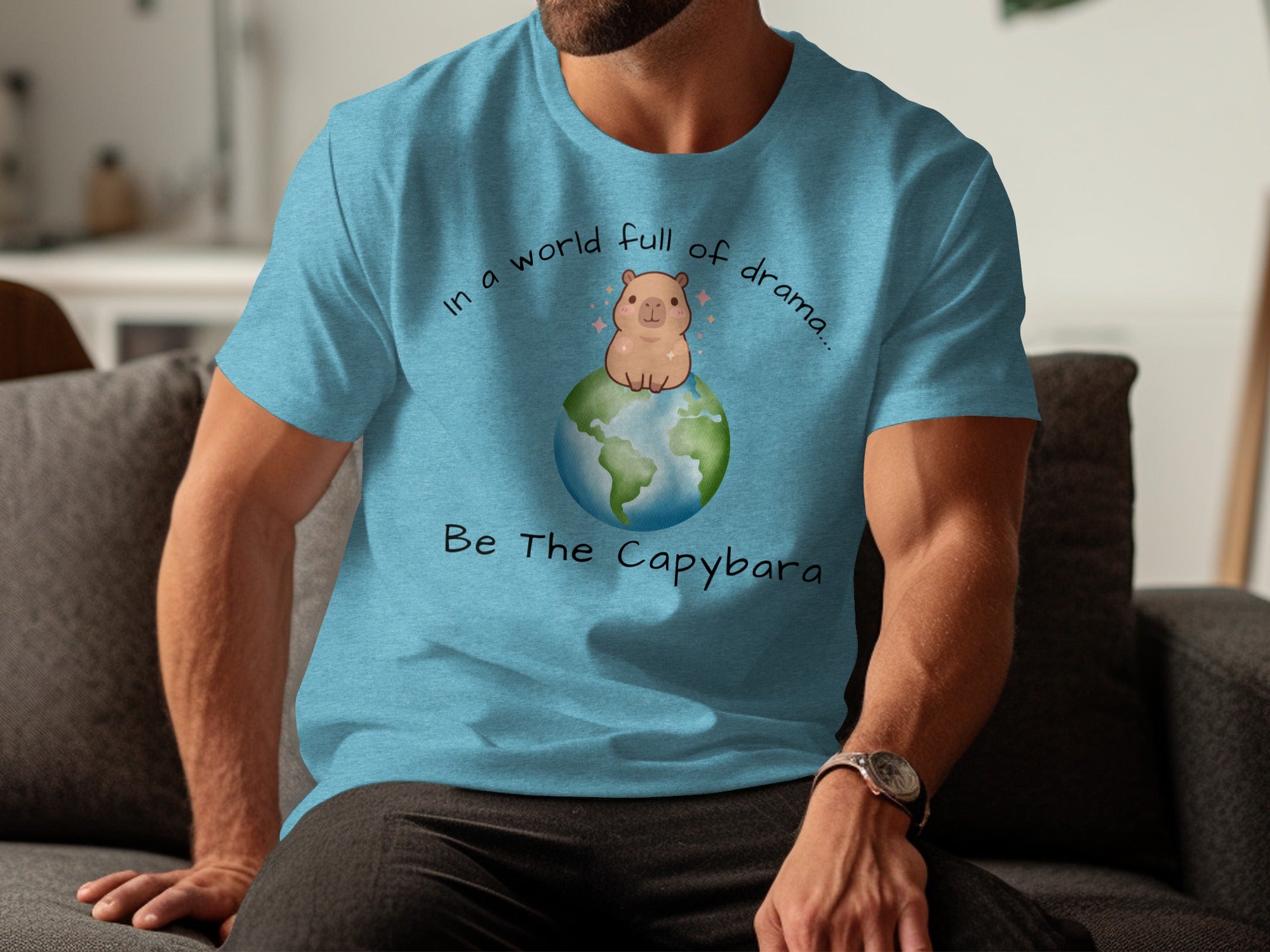 Be The Capybara text with capybara sitting on a cartoon Earth on a blue t-shirt.
